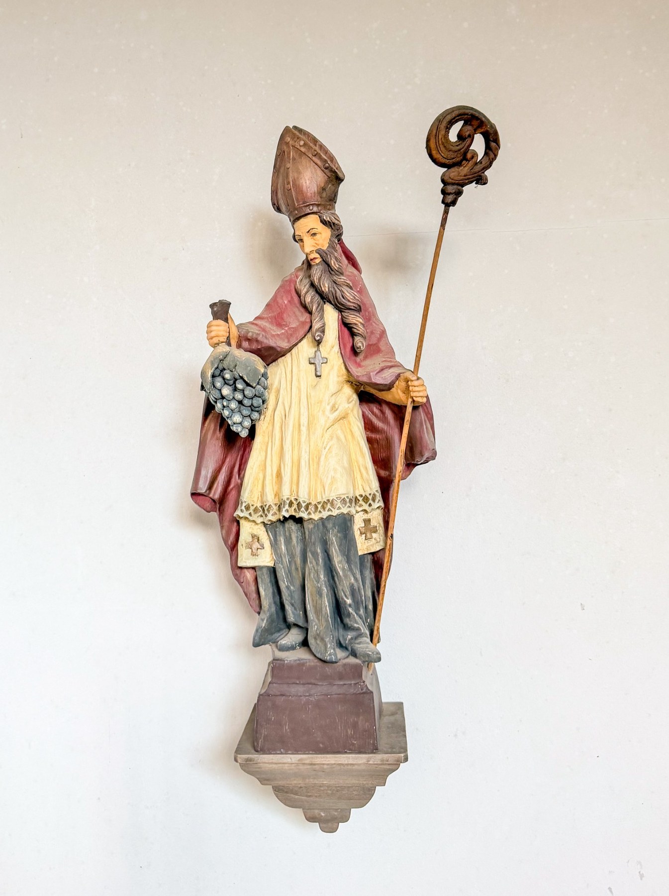 Bemalte Bischofsfigur mit Mitra, Krummstab und Weintraube.