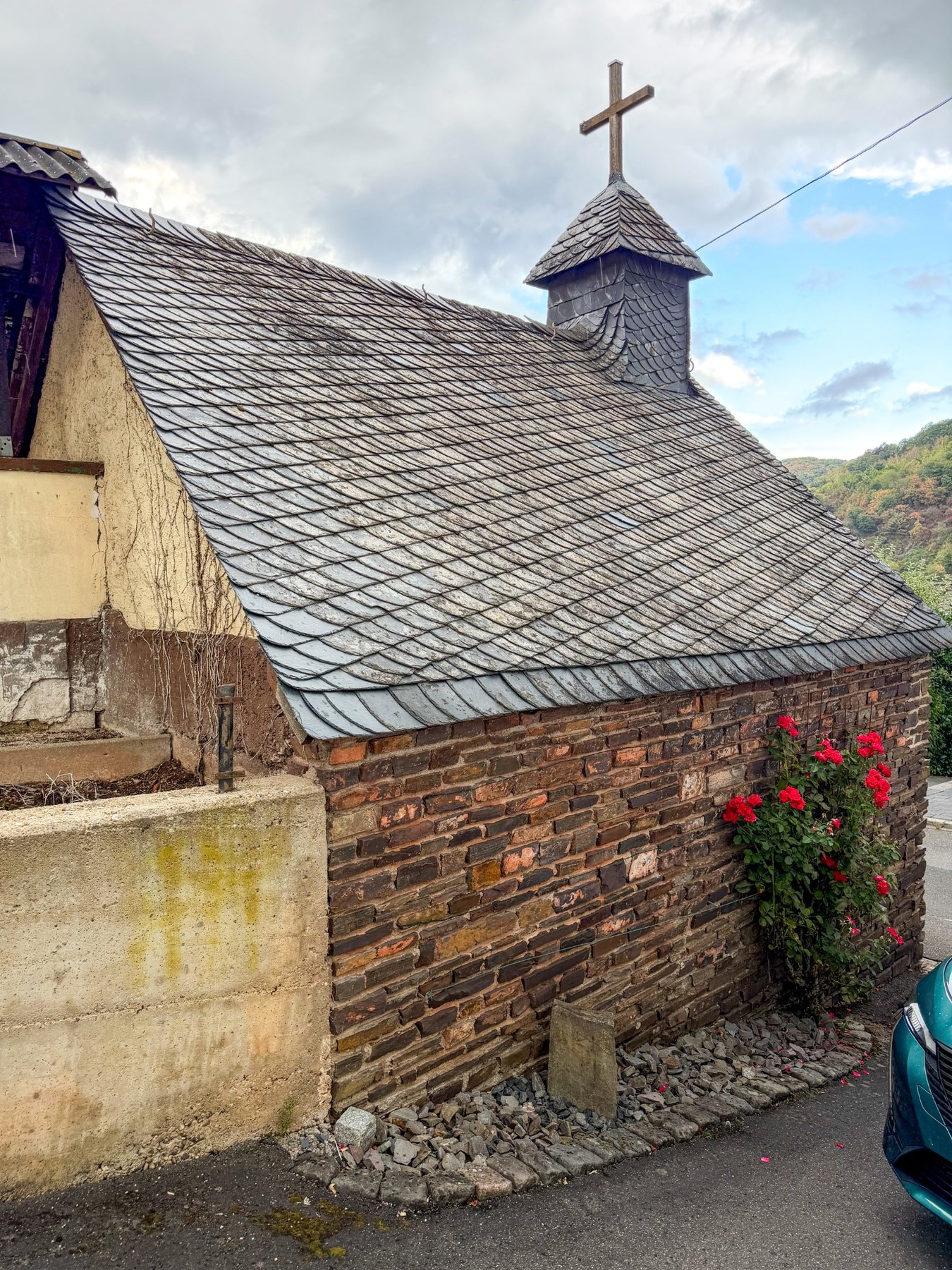 Längswand und Schieferdach der Kapelle mit kleinem Dachreiter und Kreuz.