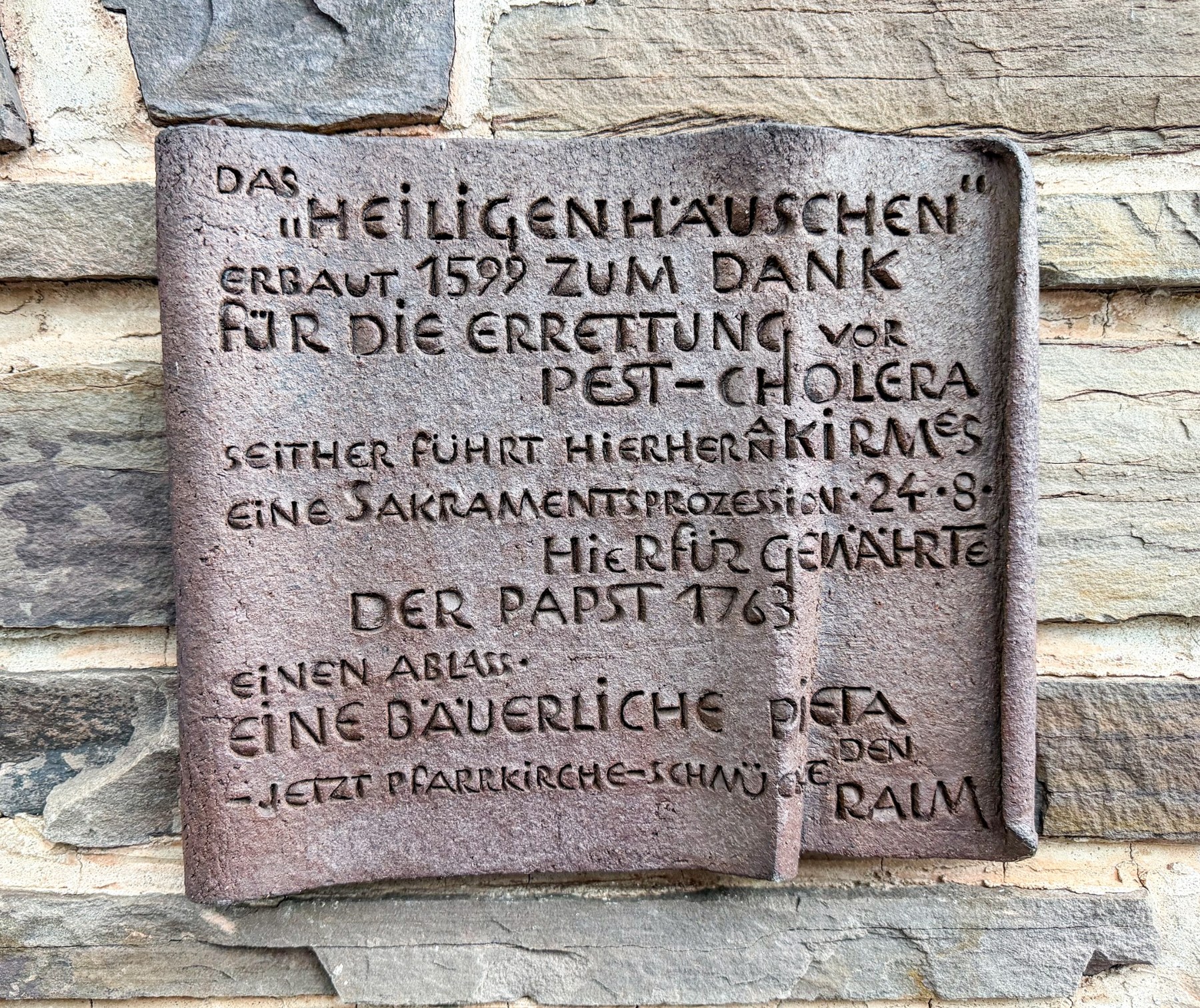 Steinerne Informationstafel an der Kapellenfassade mit Angaben zu 1599, Prozession und Ablass.
