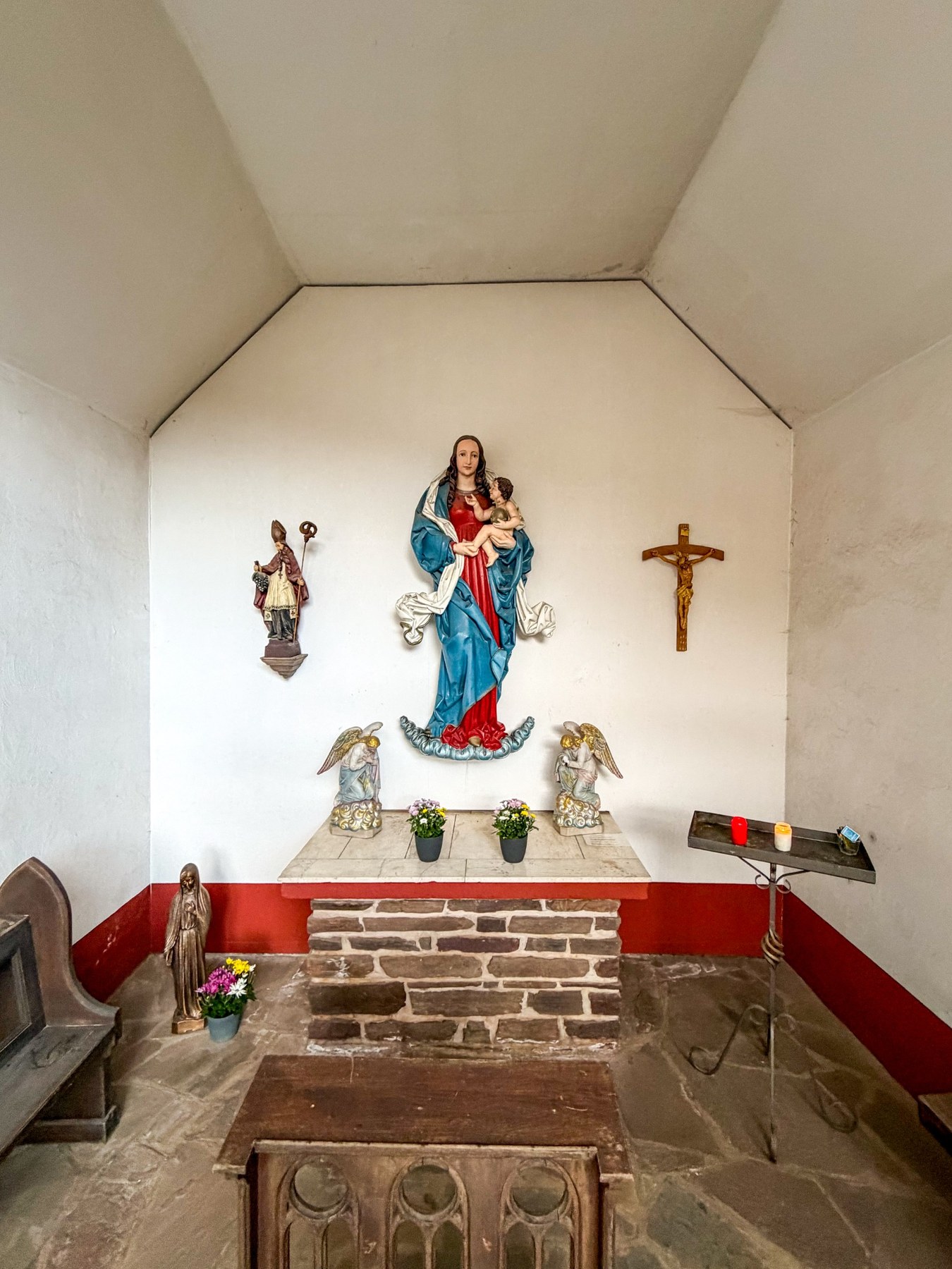 Innenraum der Kapelle mit Altar, Marienfigur, zwei Engeln, Bischofsfigur und Kruzifix.