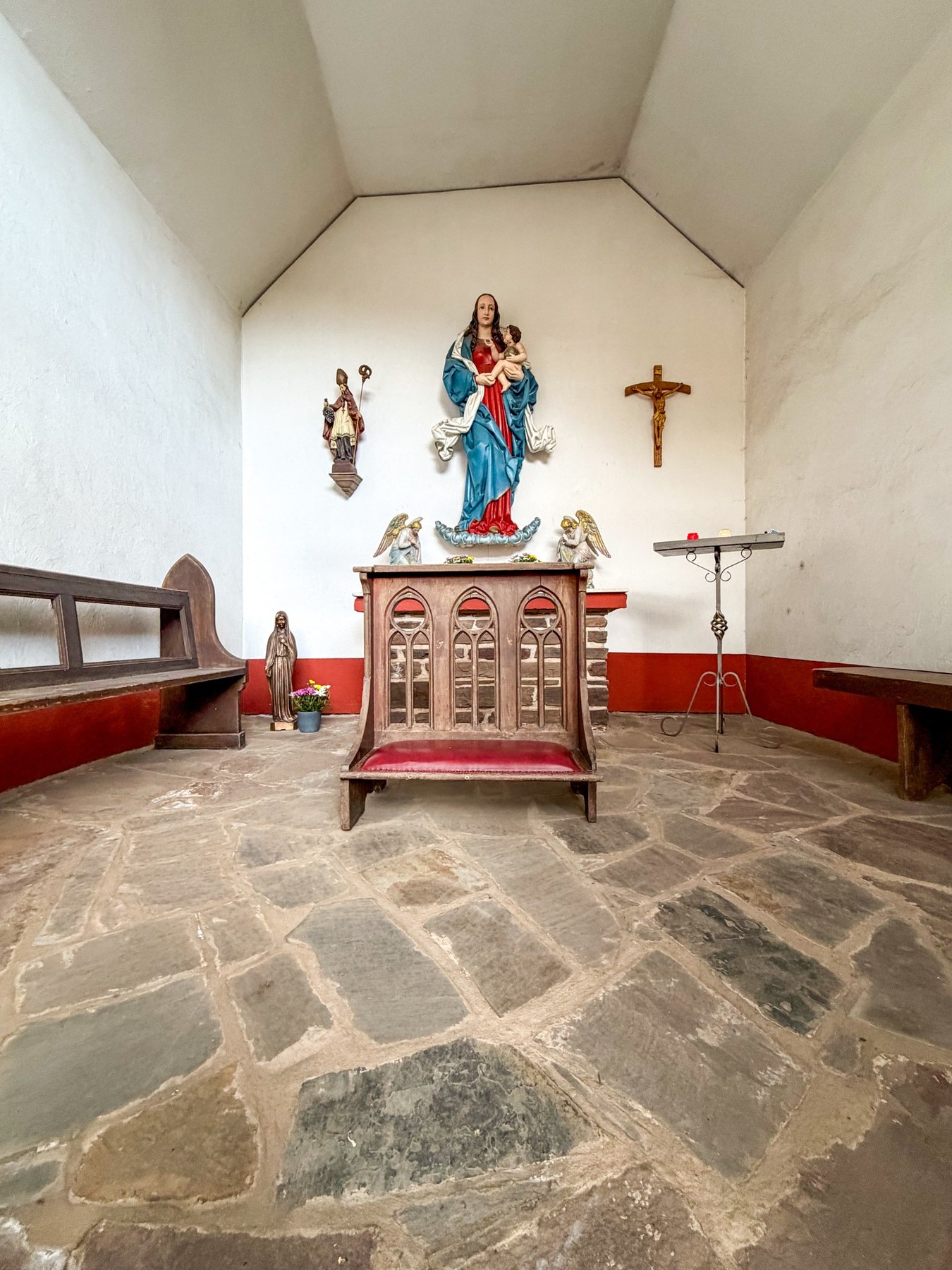Weiter Blick in den Kapellenraum mit Steinboden, Kniebank, Altar und Marienfigur.