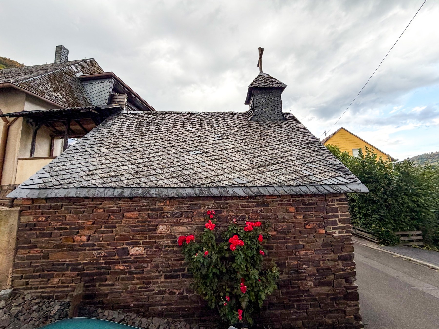 Seitliche Bruchsteinwand der Kapelle unter einem großen Schieferdach mit Dachreiter.
