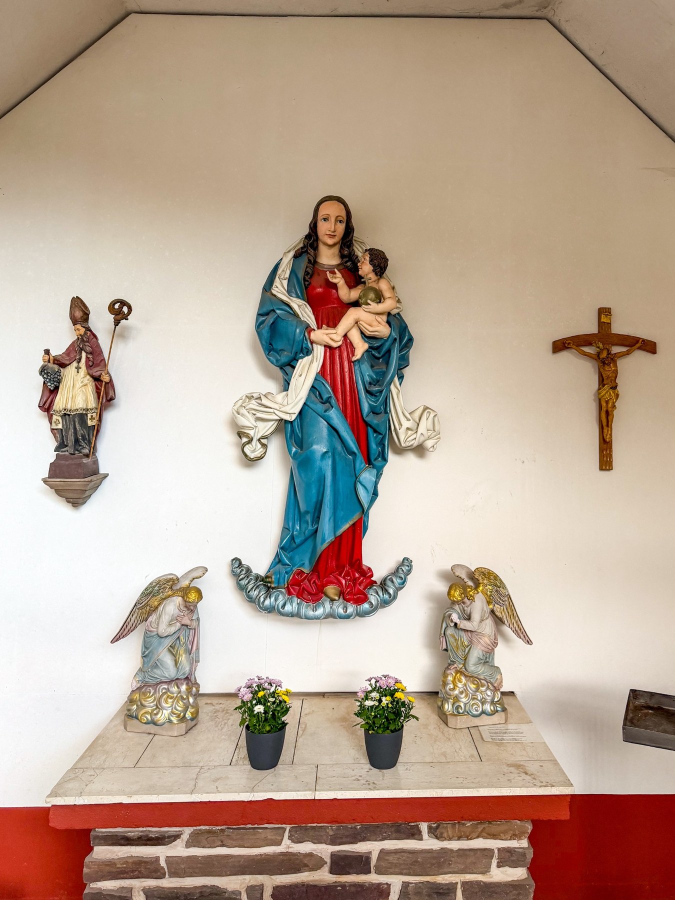 Marienfigur mit Kind auf Wolkenband über dem Altar, flankiert von zwei Engelsfiguren.